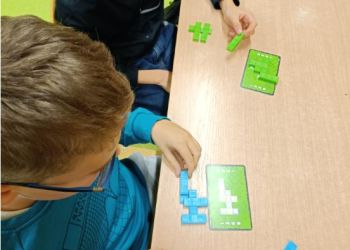 Powiększ zdjęcie: Uczniowie budują wzór pokazany na karcie z trójwymiarowych, prostokątnych klocków - utrwalają własnosci brył i figur geometrycznych.