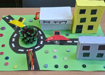 Powiększ zdjęcie: Projekt miasta przedstawiający bloki, sklep spożywczy, ulice z jadącymi samochodami i rondo.