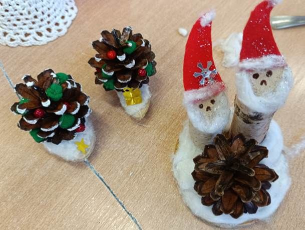 Upominki dla bliskich wykonane w ramach warsztatów - kompozycja z drewna przedstawiająca dwa mikołaje wokół choinki i buty z szyszek oraz drewna.