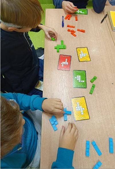 Uczniowie budują wzór pokazany na karcie z trójwymiarowych, prostokątnych klocków.