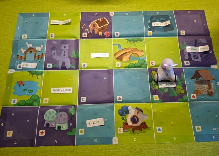 Robot Photon na macie obok zadania dotyczącego rachunków pamięciowych 4ꞏ1200, 70000-25000, 9ꞏ110000, 6300:3, 5700000:1000, 4500+3500 i 240000+160000.