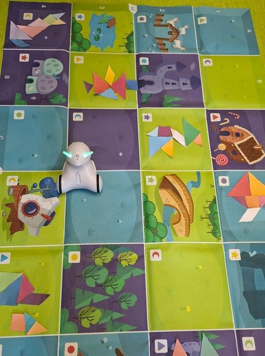 Robot Photon na macie z ułożonymi figurami z dostępnych części tangramów.